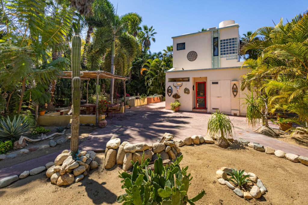 Todos Santos La Cachora Charming Tropical Beachside Retreat in Todos Santos. Nestled in the sought-after La Cachora seaside community of Todos Santos, this enchanting property is located at the end of a serene cul-de-sac on Brock Lane, named after the builder of the charming homes in the neighborhood. This residence beautifully combines traditional Mexican architectural elements with a modern twist, highlighted by a remodeled kitchen that caters to contemporary tastes.The main house features 1 bedroom and 1.5 baths, designed for comfort and functionality. Surrounded by inviting palapa shade porches, the exterior space offers an ideal setting for relaxation and entertaining, seamlessly blending indoor and outdoor living. A quaint palapa serves as a multifunctional art studio, adding a creative workshop space to the property. The second structure a more contemporary studio casita. Complete with a full bath, kitchenette, and a rooftop hammock deck overlooking the lush surroundings, this studio is perfect for guests or as a rental opportunity. The deck also features a palapa, and a swimming pool, providing a delightful space for leisure. Profoundly landscaped gsardens are a true highlight, featuring a rich array of fruit trees, cacti, agaves, pomegranates, and aloe, along with mature exotic palms. Park-like Setting**: Meandering footpaths connect the main house to the garden and the studio casita, creating a magical, private oasis that feels like a tranquil retreat. The home is within a short, leisurely walk to La Cachora beach, ensuring easy access to the mighty Pacific and local attractions. This tropical paradise offers peace of mind in a stunning environment, ideal for those seeking a blend of artistic inspiration and serene living. Whether utilized as a primary residence, guest accommodations, or rental income, this property exemplifies the charm and allure of Todos Santos living. – La Cachora North, Pacific, BS